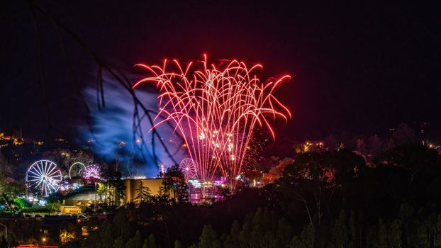 Spectacular fireworks display lighting up the sky above an amusement park at night.