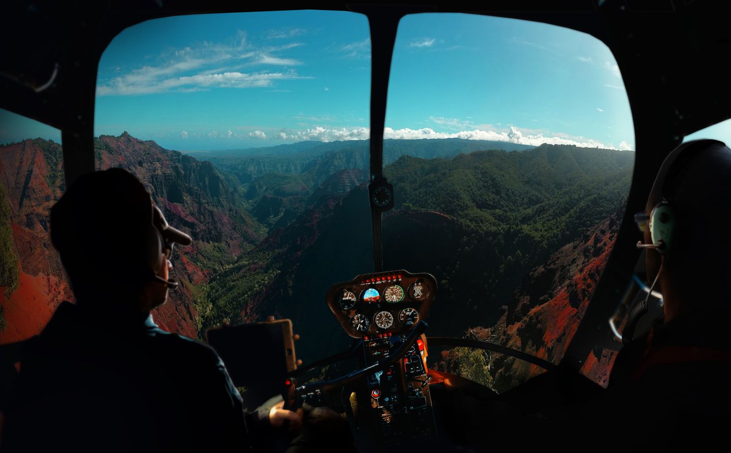 The view forward from a helicopter cockpit over the green valleys of Kauaʻi