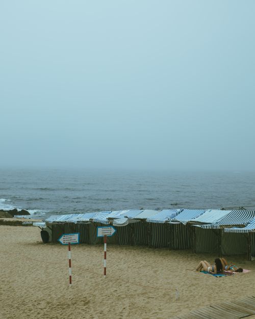Free A foggy beach with striped tents lining the shore and a moody sea view, evoking a serene atmosphere. Stock Photo