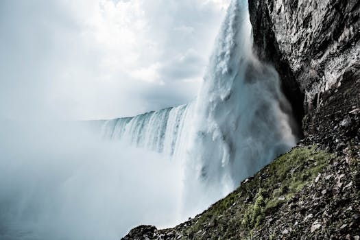 Stunning waterfall plunging off a cliff surrounded by mist and rocky terrain under a cloudy sky.