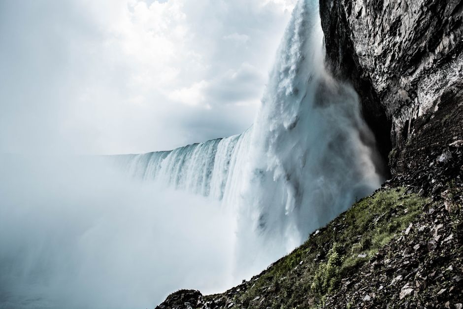 Stunning waterfall plunging off a cliff surrounded by mist and rocky terrain under a cloudy sky.