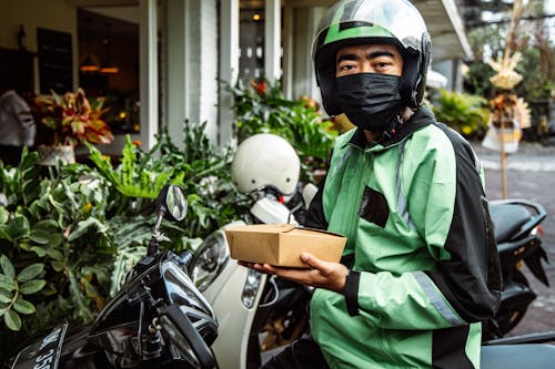 A Man In Black and Green Jacket Holding a Box of Food
