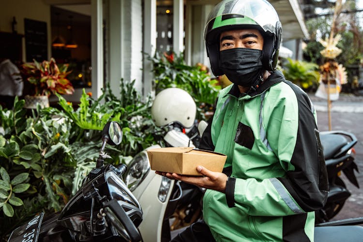 A Man In Black And Green Jacket Holding A Box Of Food