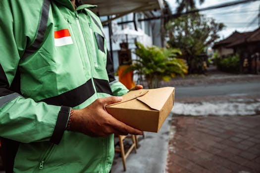 A person in a green jacket delivering a package outdoors. Urban setting, daytime.