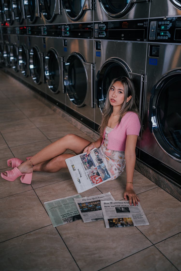 Woman Sitting On The Floor In A Laundry Facility And Holding Newspapers 