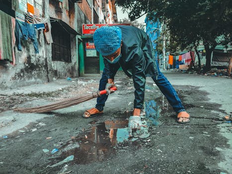 A person wearing a mask and gloves cleaning the street in a Bangladesh neighborhood.