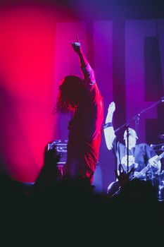 Energetic concert scene with performers on stage under vibrant red and blue lights.