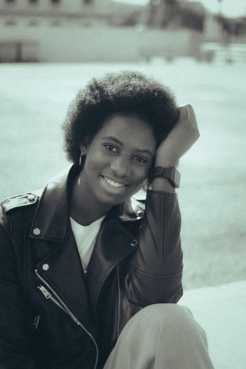 Free Monochrome portrait of a smiling woman with afro hair in a leather jacket outdoors. Stock Photo