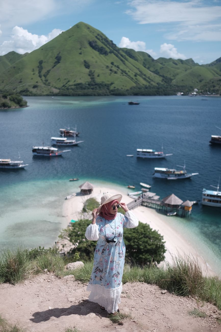 Tourist overlooking Pulau Kelor, East Nusa Tenggara, with lush hills and sea in the background.