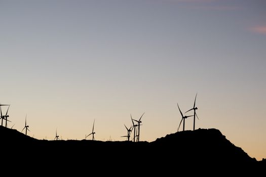 Silhouette of wind turbines against a serene sunset sky, symbolizing renewable energy.