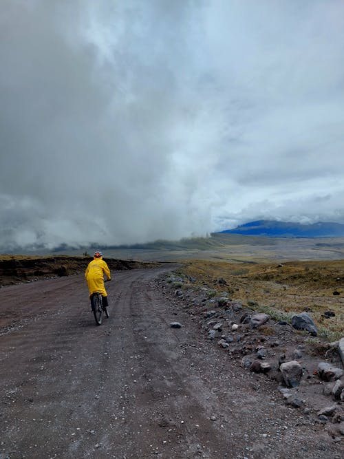 Cyclist in Yellow Raincoat Riding on Wide Gravel Road Through the Countryside