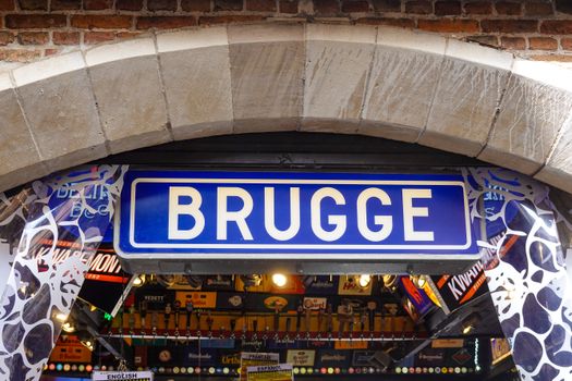 Sign marking entrance to a shop in Bruges, Belgium, featuring classic brick archway architecture.