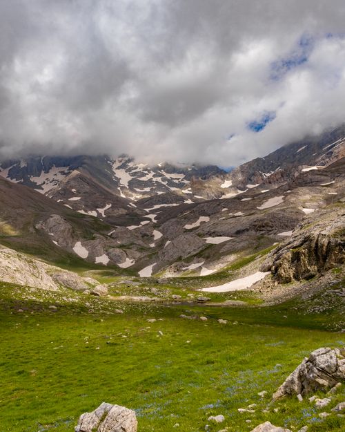 Free Stunning view of alpine mountains with patches of snow and lush grass under a cloudy sky. Stock Photo