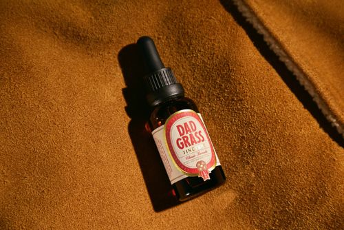 Free Close-up of CBD oil tincture bottle labeled 'Dad Grass' on brown fabric background. Stock Photo