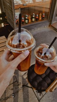 Two hands holding iced coffee with straws outside a Kyiv cafe. Summery vibe.