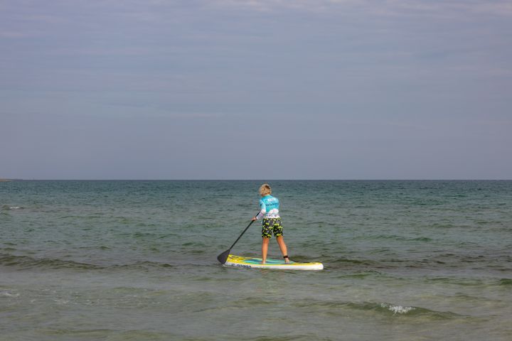 Person paddleboarding on a calm sea under a clear sky, enjoying outdoor recreation.