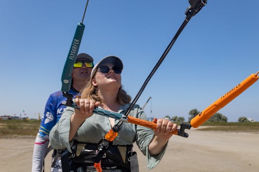 Woman learning kitesurfing with an instructor on a sunny beach day.