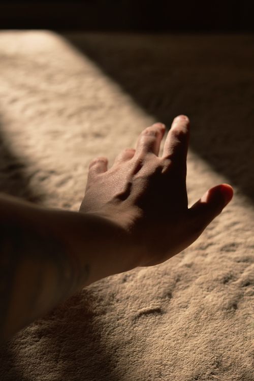 Free A close-up of an adult hand reaching out on a textured surface with dramatic sunlight. Stock Photo