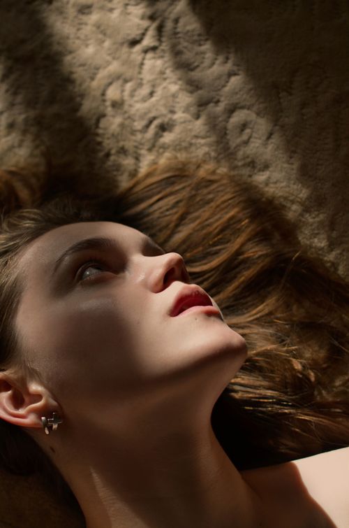 Free Close-up of a young woman lying down, captured with dramatic lighting and shadow play. Stock Photo