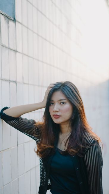 Portrait of a young woman in Indonesia posing by a sunlit tiled wall, exuding confidence.