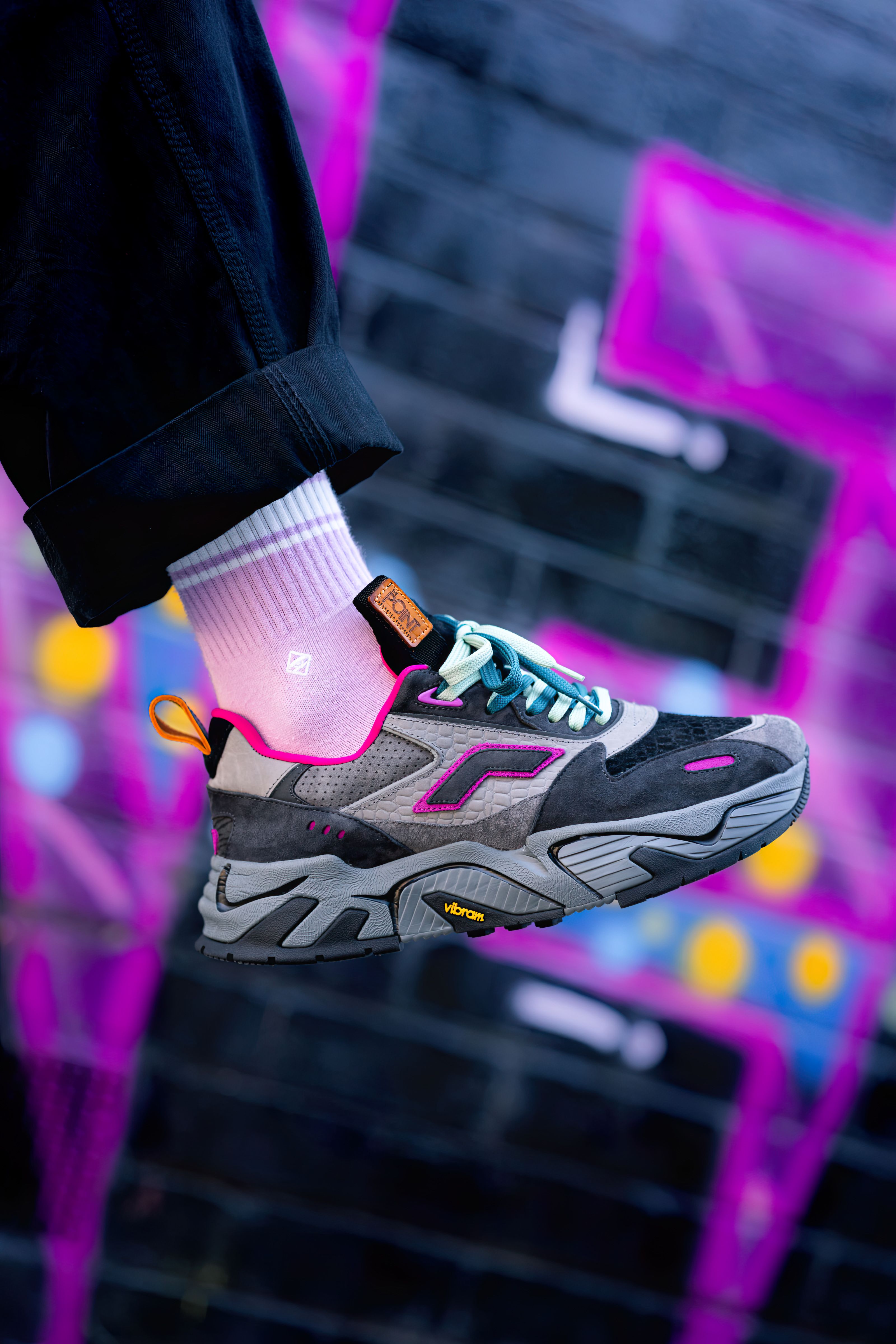 Vibrant sneaker with pink accents against a graffiti wall, showcasing street fashion.