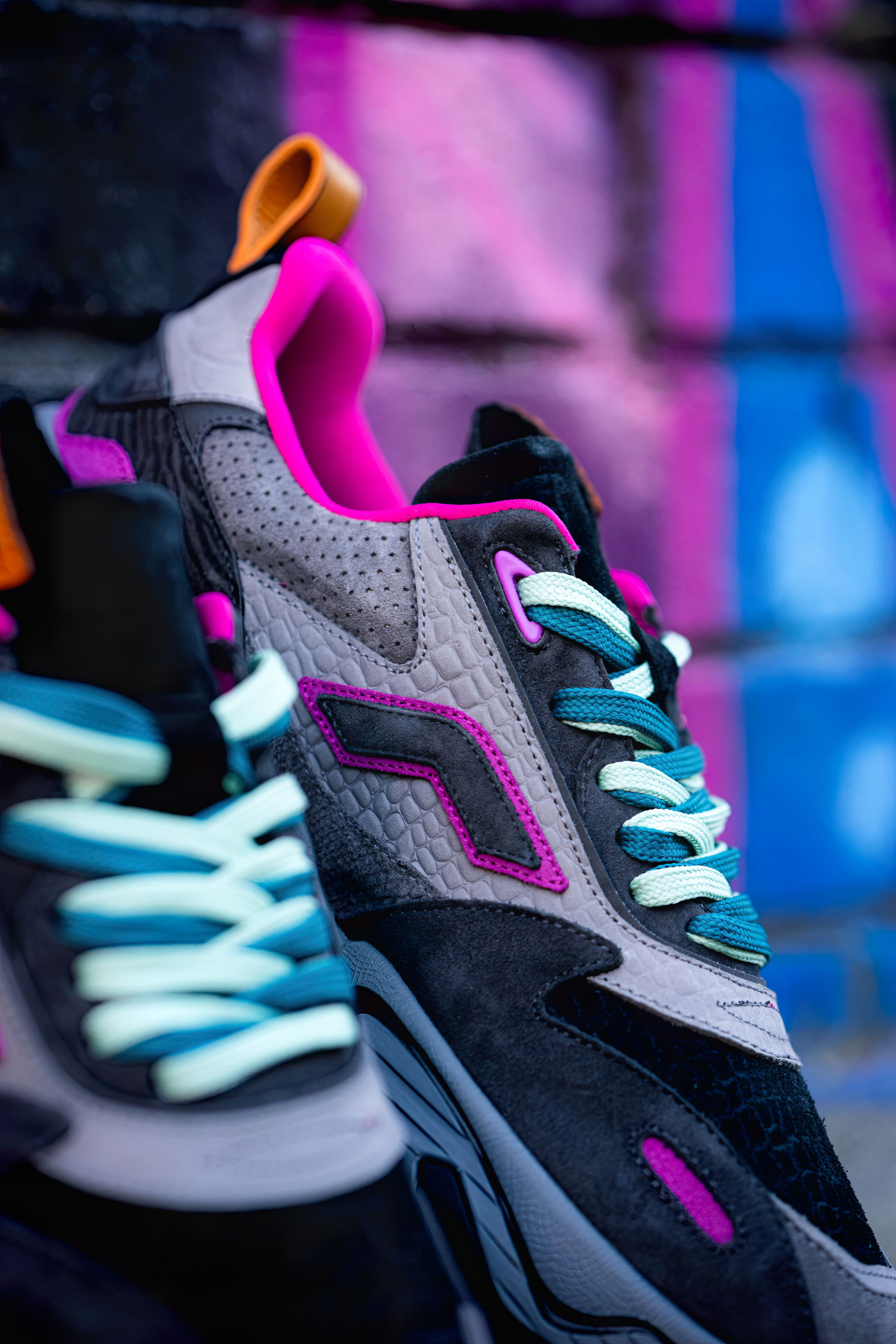 Colorful sneakers with neon accents against a vibrant graffiti wall.