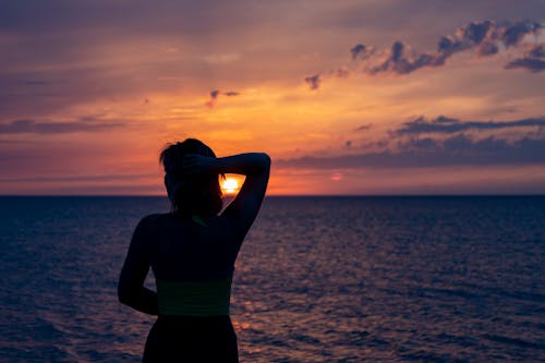 A Woman in Green Tank Top Standing on Beach during Sunset
