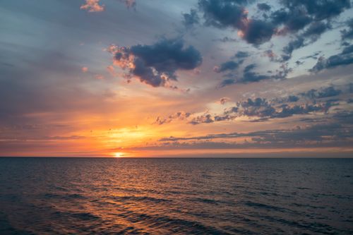 Free Breathtaking view of the ocean at sunset with vibrant colors and dramatic clouds. Stock Photo