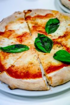 Close-up of a freshly baked Margherita pizza with cheese and basil on a ceramic plate.