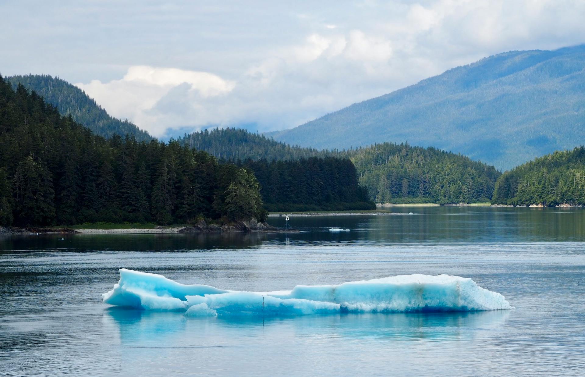 Breathtaking Alaskan fjord view with floating iceberg reflecting in calm waters.