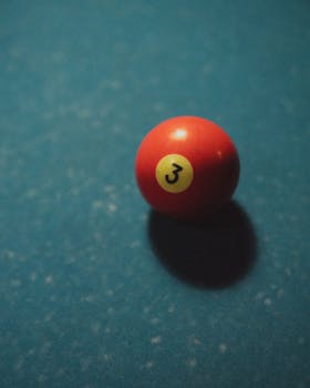 Close-up of a red billiard ball on a blue pool table, showcasing the number three.