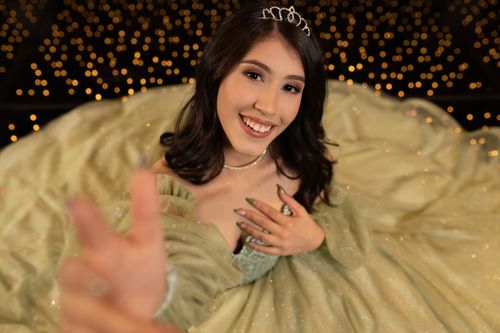Free A beautiful young woman in a tiara smiling and posing in a glamorous gown, captured in an elegant setting. Stock Photo