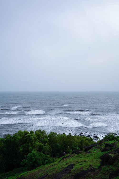 Free Serene seascape with storm clouds over waves and green cliffside, providing a captivating nature view. Stock Photo