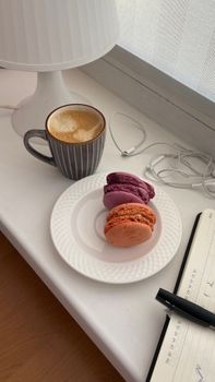 Warm morning scene with coffee and colorful macarons on a table.
