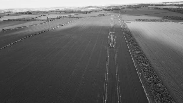 Black and white aerial photo of power lines crossing rural fields, creating geometric patterns.