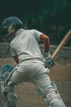 A young male cricketer wearing full gear, ready to bat on an outdoor field.