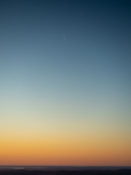 A calm twilight sky with a crescent moon and gradient colors from orange to blue.