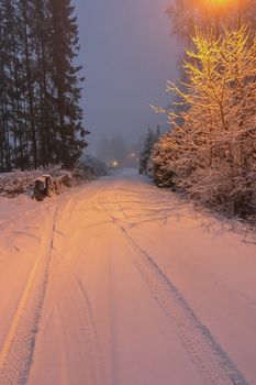 A serene snowy road at dusk illuminated by a warm streetlight, showcasing winter's tranquil beauty.