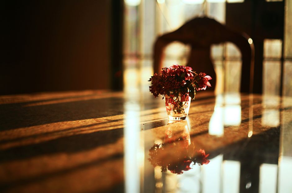 A sunlit bouquet in a vase placed on a reflective wooden table, capturing warm indoor ambiance.