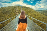 一名妇女走在廊桥上，两旁是郁郁葱葱的森林和风景优美的山丘