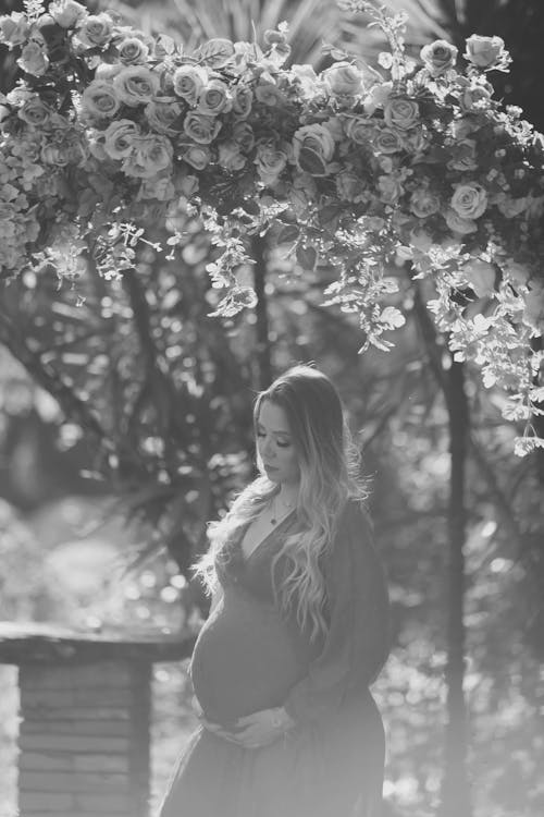 Photo of a Standing in a Garden Pregnant Woman Keeping Hand under a Belly 