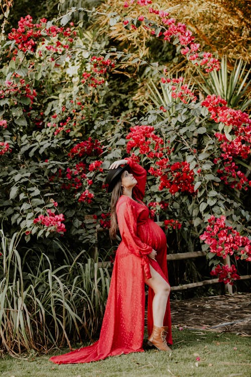 Pregnant Woman in Red Dress Posing among Flowers and Bushes