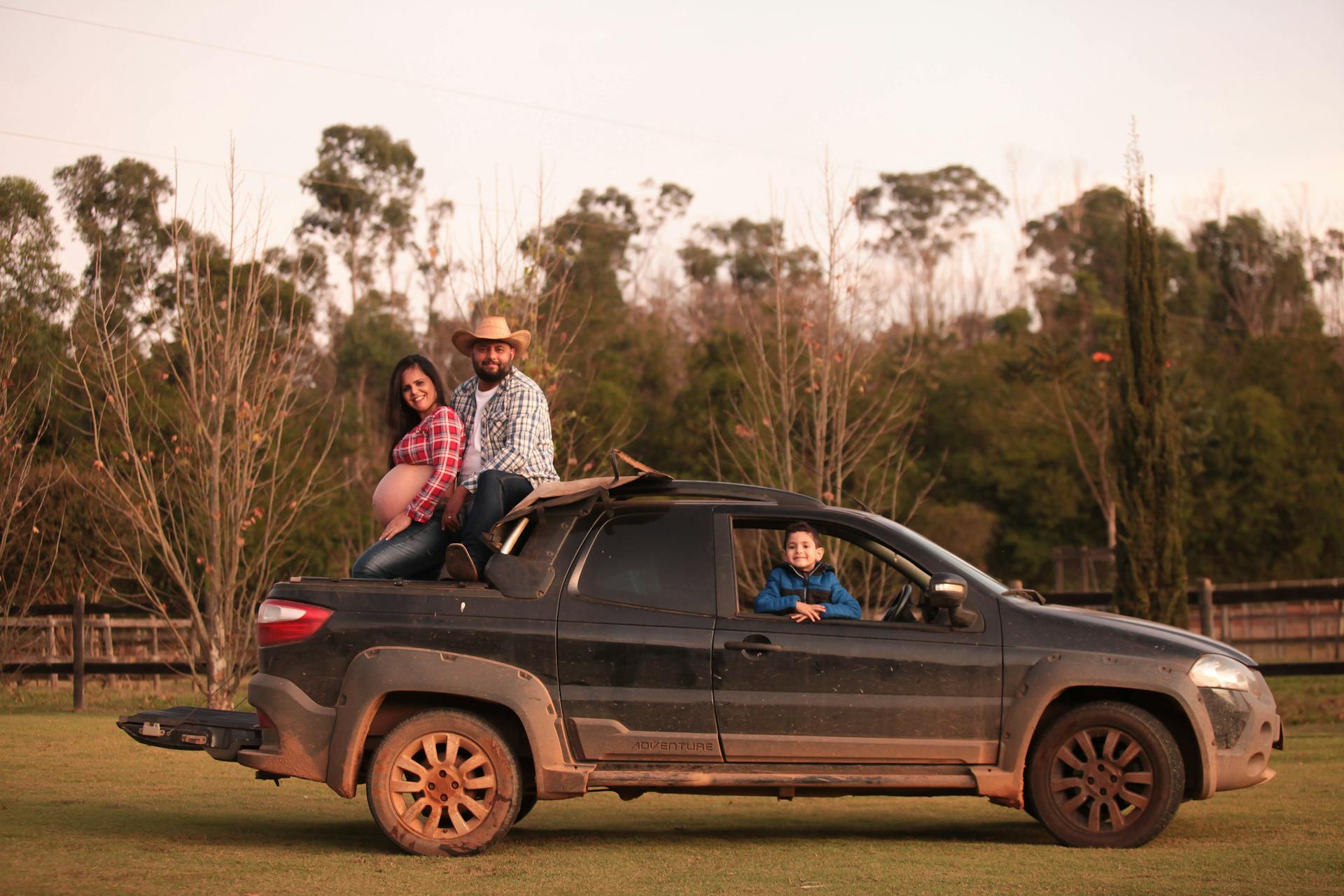 Smiling family enjoying a sunny day on a muddy pickup truck in the countryside.