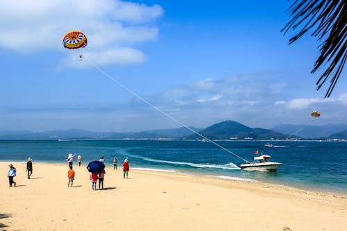 People Parachuting behind Motorboat on Sea Shore