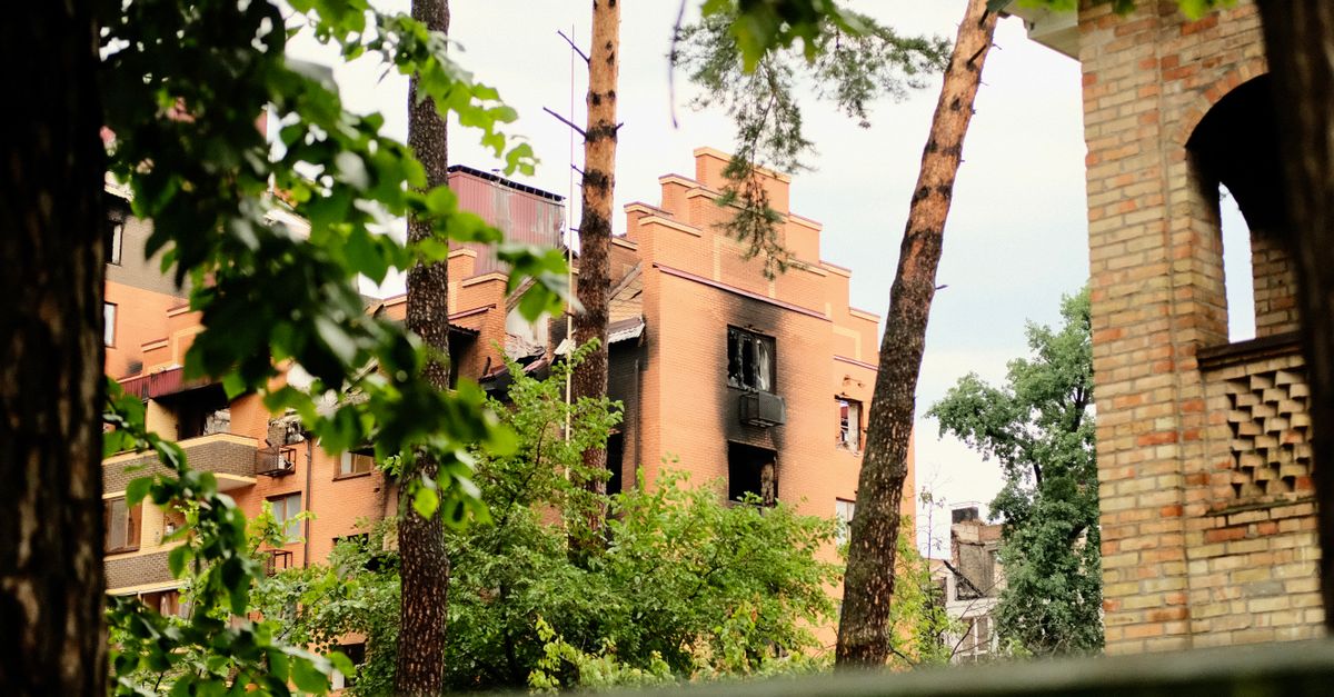 A damaged residential building, charred by fire, stands among lush trees in an urban setting.