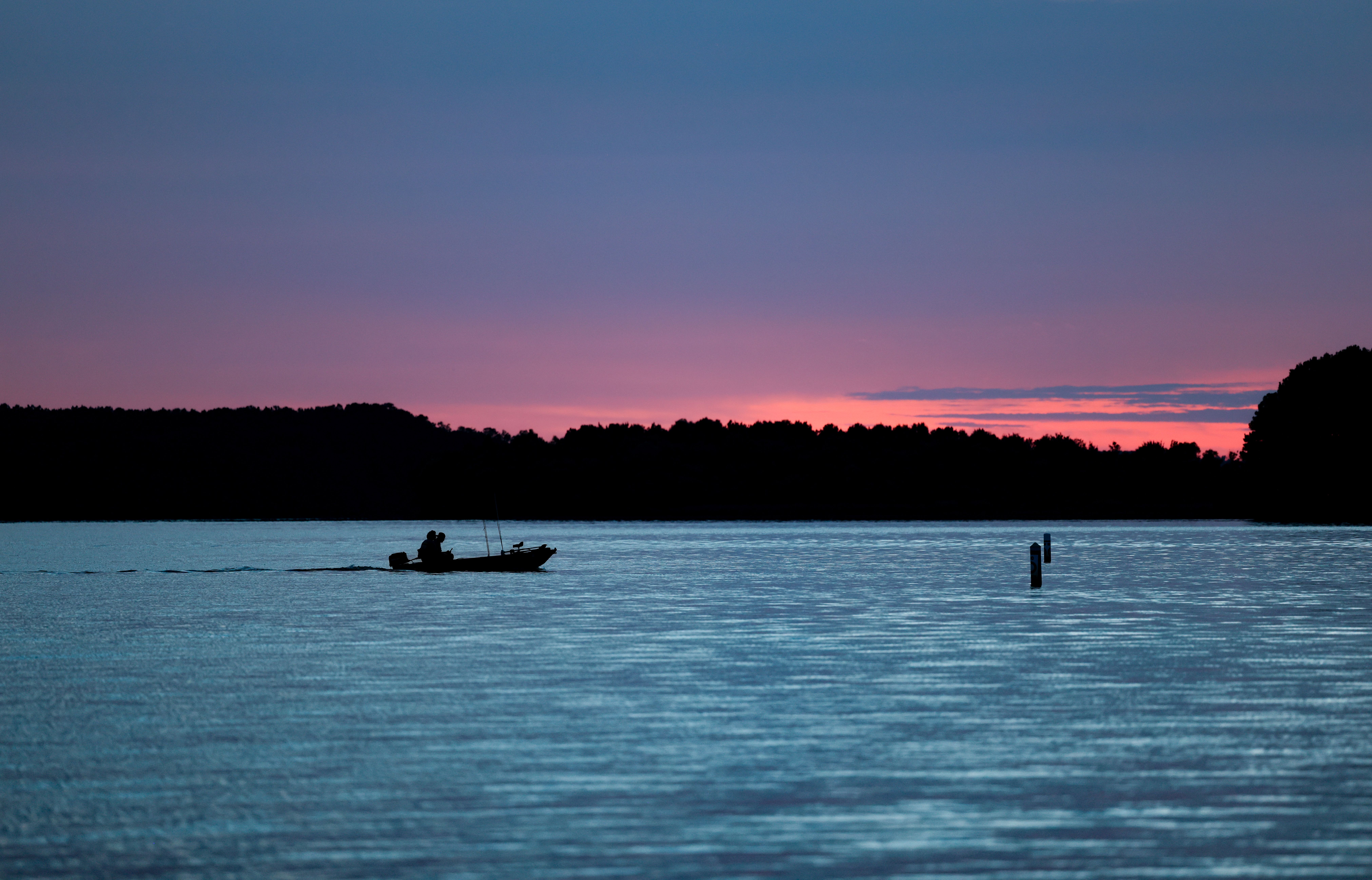 Silhouette of a boat on a serene lake at sunset with a stunning purple sky.