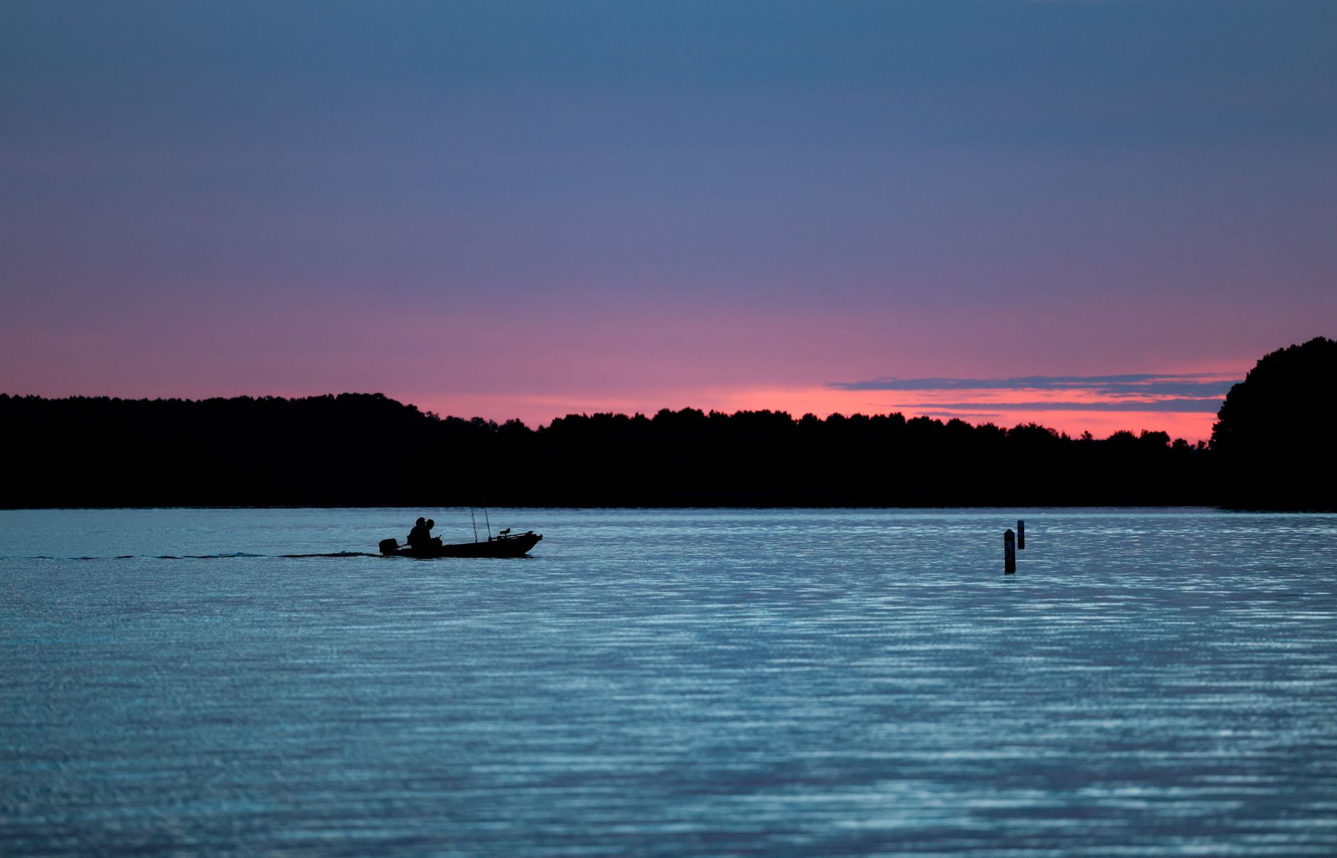 Silhouette of a boat on a serene lake at sunset with a stunning purple sky.