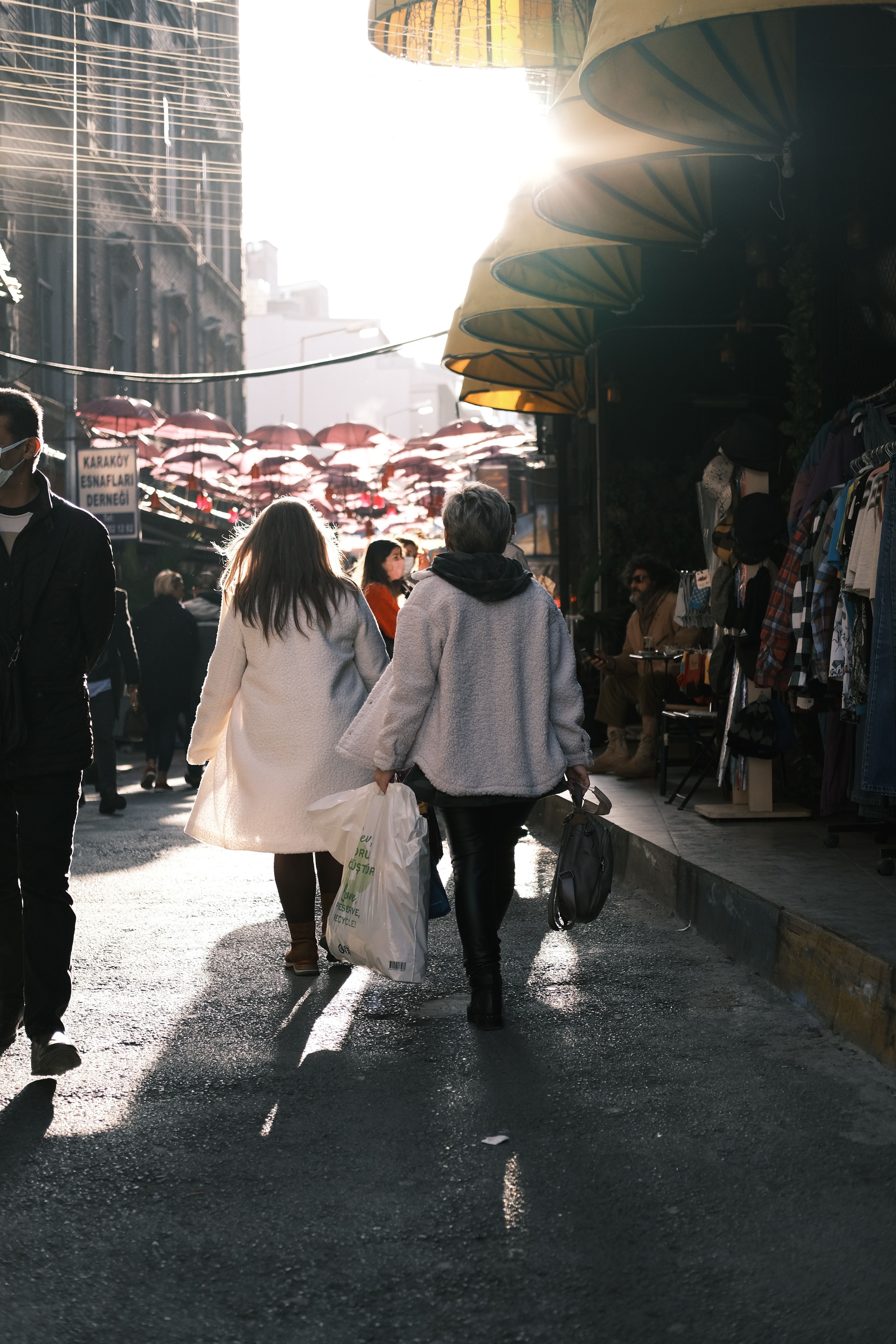 People walking in a sunlit market street in Istanbul, contrasting light and shadow.