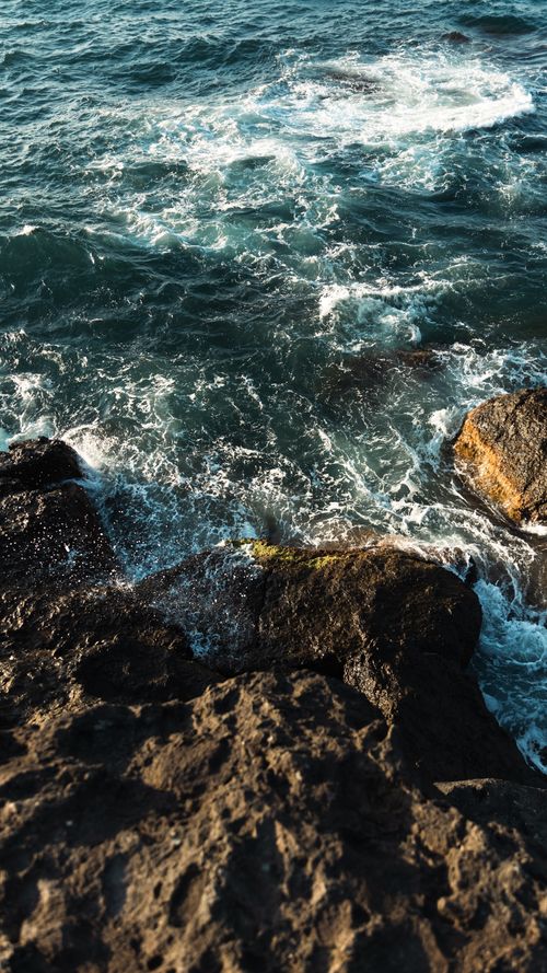 Free Dramatic view of waves crashing onto a rocky seashore with vibrant ocean water. Stock Photo