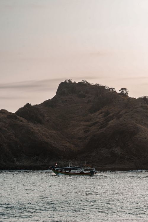 Free A peaceful scene of a boat sailing near an island with a mountainous backdrop. Stock Photo